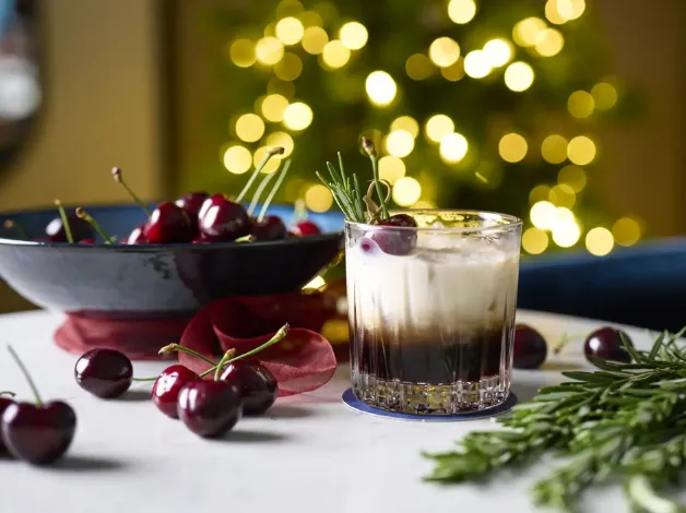 Festive cocktail with cherries and rosemary, bokeh background.